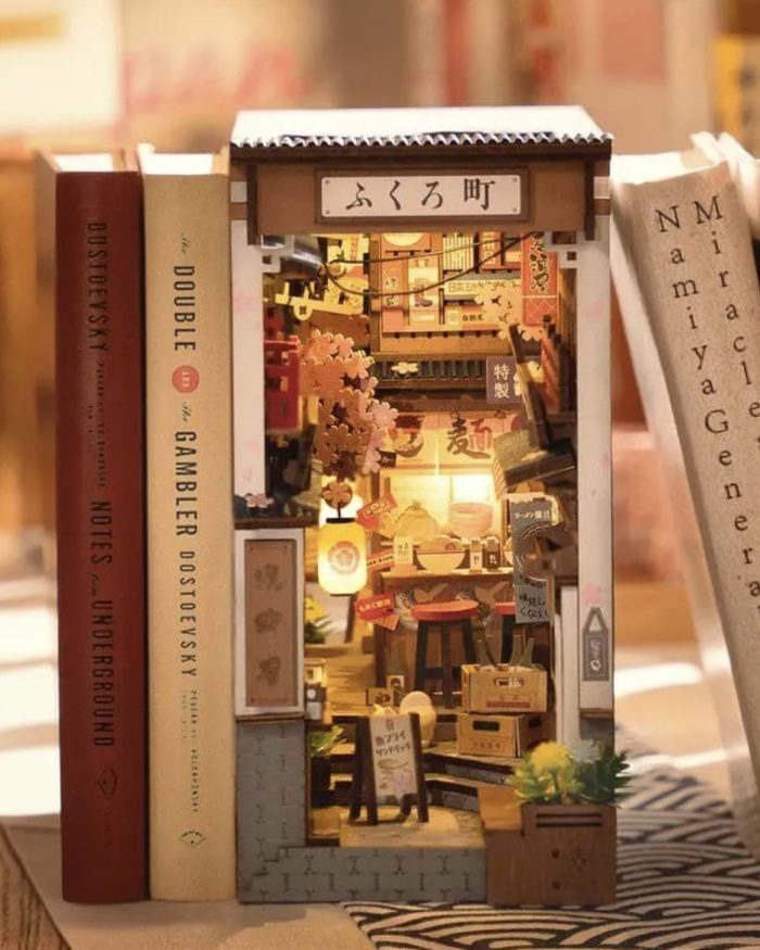 A built book nook: a lit laneway scene standing between books on a shelf