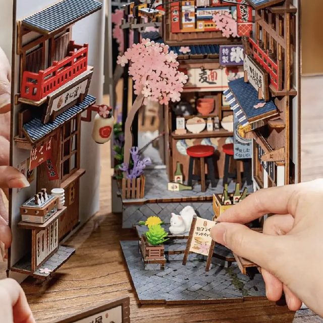 Hands placing a tiny sign into the book nook scene